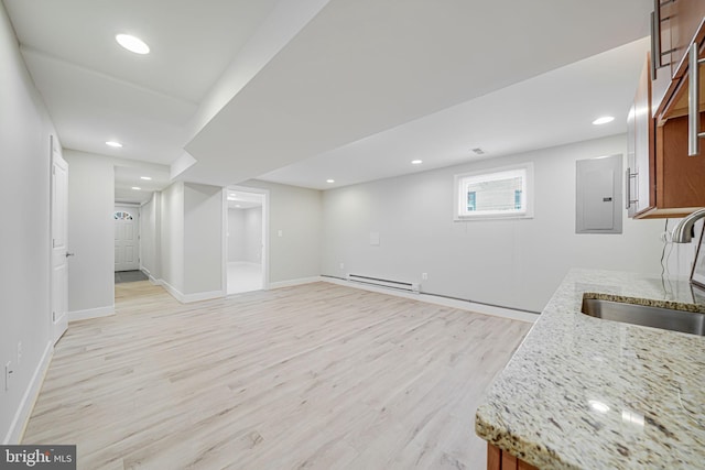 below grade area featuring light wood finished floors, a sink, baseboards, electric panel, and a baseboard radiator