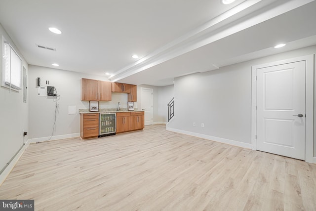 kitchen with brown cabinetry, beverage cooler, visible vents, light countertops, and light wood-style floors