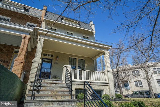 view of front of home with a porch, stairway, mansard roof, and brick siding