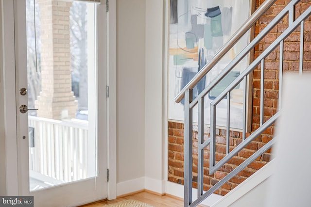 staircase with wood finished floors, baseboards, and brick wall