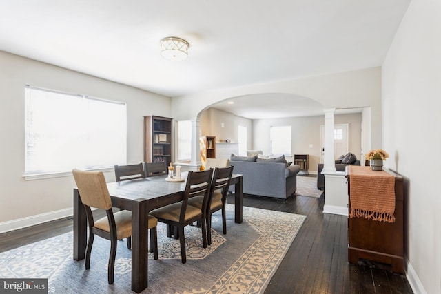 dining room featuring decorative columns, arched walkways, dark wood finished floors, and baseboards