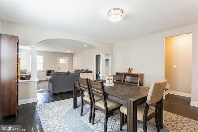 dining room featuring arched walkways, dark wood-style floors, decorative columns, and baseboards