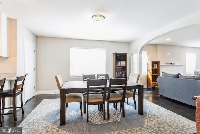 dining room with dark wood-style floors, baseboards, arched walkways, and ornate columns