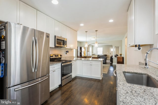 kitchen with arched walkways, appliances with stainless steel finishes, open floor plan, a peninsula, and a sink