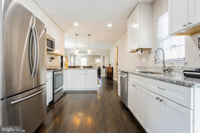 kitchen featuring appliances with stainless steel finishes, dark wood-type flooring, open floor plan, a sink, and a peninsula