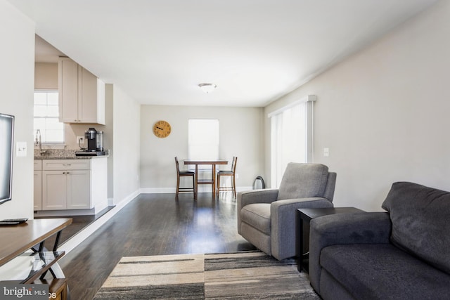 living room featuring baseboards, dark wood-style flooring, and a healthy amount of sunlight