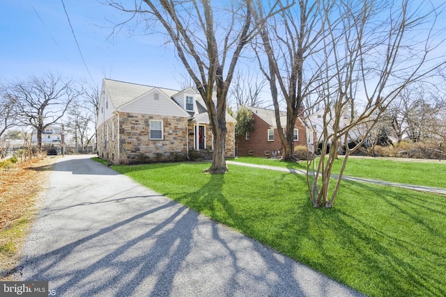 view of front facade with stone siding, driveway, and a front lawn