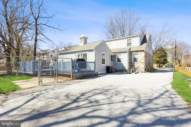 view of front of house featuring stone siding, a gate, fence, and roof with shingles