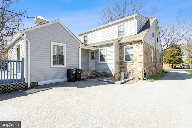 back of property featuring stone siding and roof with shingles