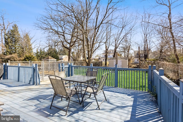 wooden terrace featuring a storage shed, a fenced backyard, an outbuilding, outdoor dining area, and a yard