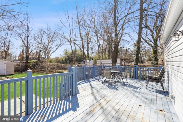 deck featuring outdoor dining area, a fenced backyard, an outdoor structure, a yard, and a shed