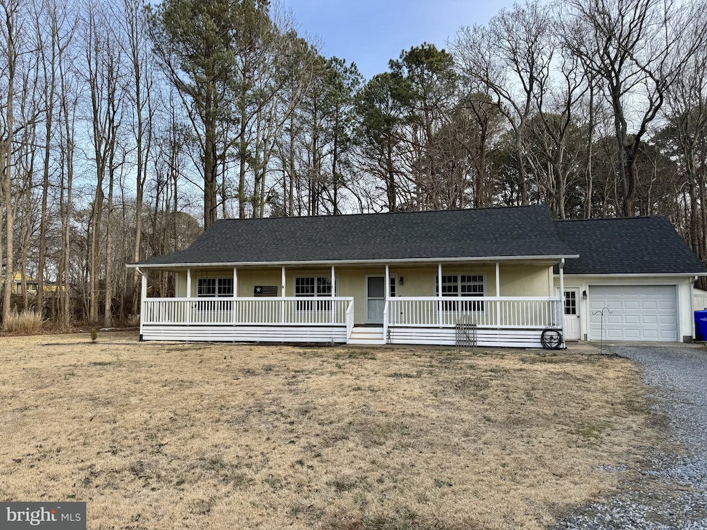 single story home with covered porch, a shingled roof, gravel driveway, and a garage