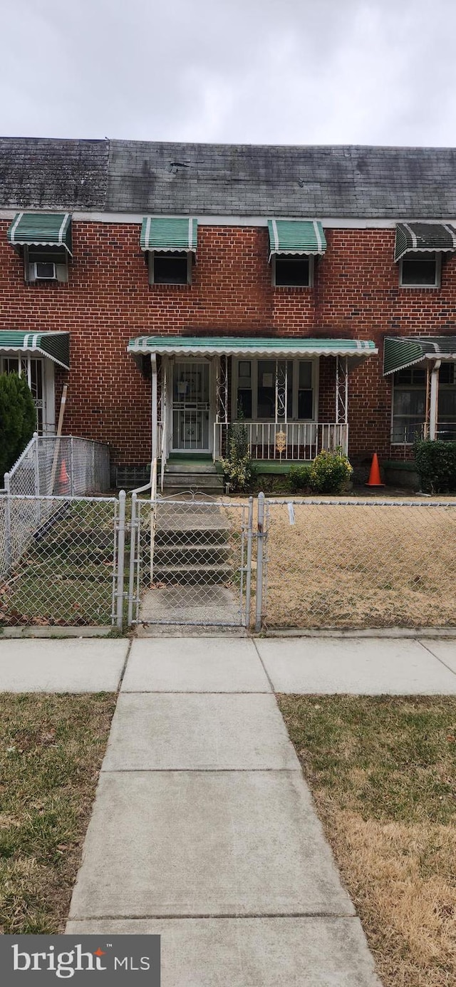 multi unit property with a fenced front yard, a gate, brick siding, and mansard roof