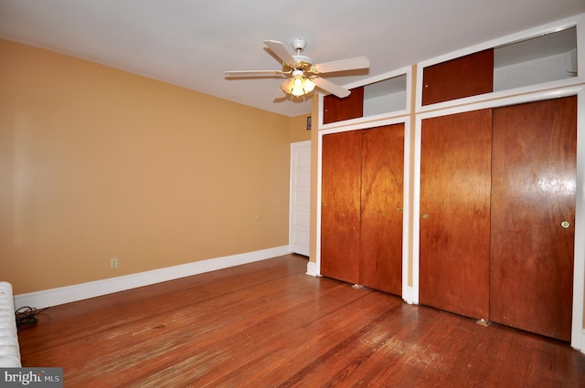 unfurnished bedroom with a ceiling fan, baseboards, two closets, and wood finished floors