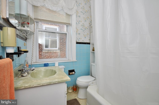 full bathroom featuring wallpapered walls, wainscoting, toilet, vanity, and tile walls