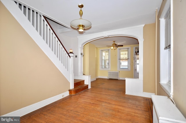 entrance foyer featuring arched walkways, stairs, light wood-style flooring, and radiator