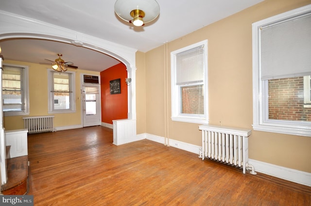 spare room featuring arched walkways, baseboards, wood finished floors, and radiator