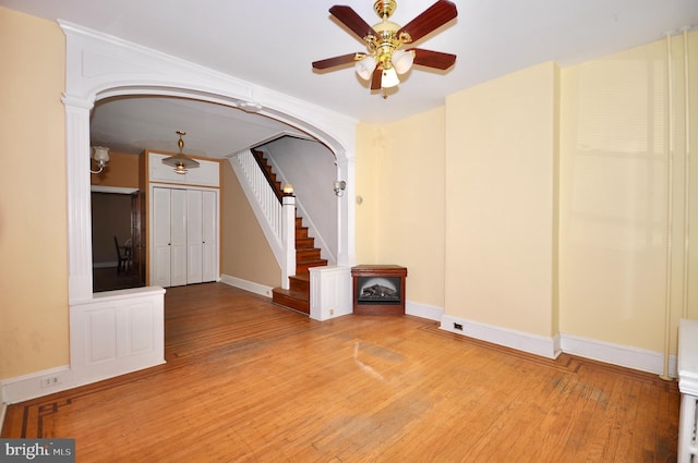 empty room with arched walkways, ceiling fan, stairway, and wood finished floors