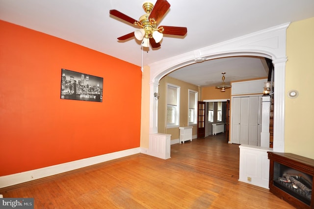 interior space with arched walkways, wood finished floors, baseboards, radiator, and radiator heating unit