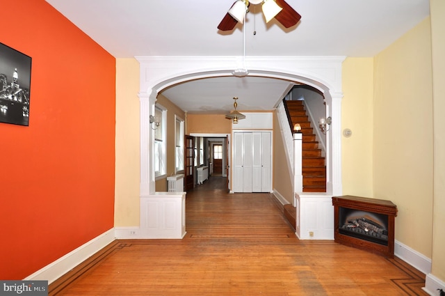 corridor featuring arched walkways, wood finished floors, stairs, and baseboards