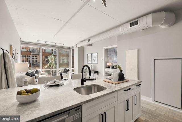 kitchen featuring track lighting, a sink, open floor plan, white cabinetry, and light stone countertops