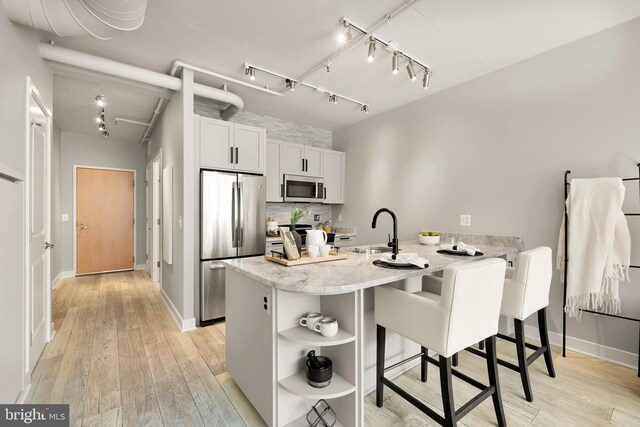 kitchen featuring light wood finished floors, open shelves, appliances with stainless steel finishes, a peninsula, and a sink