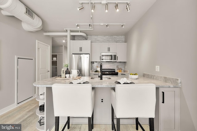 kitchen with light wood finished floors, a breakfast bar area, decorative backsplash, stainless steel appliances, and a sink