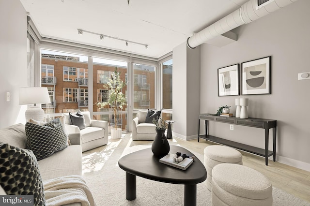 living area featuring track lighting, a wall of windows, baseboards, and wood finished floors