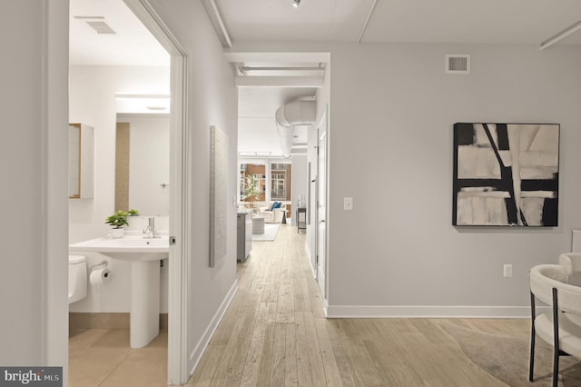 corridor featuring visible vents, baseboards, and light wood-style floors