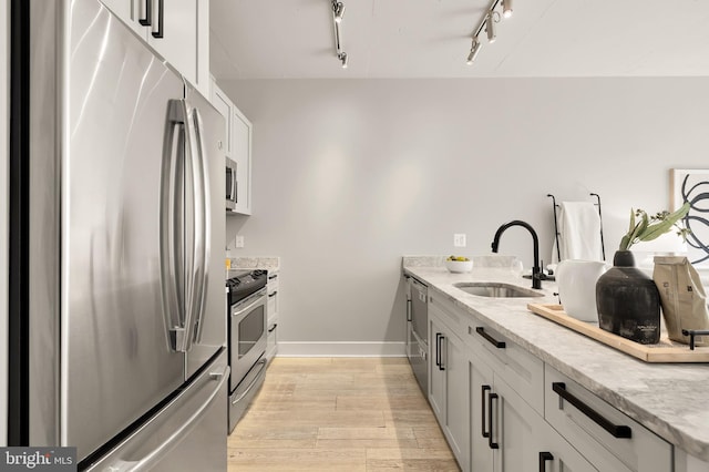 kitchen with light wood-style flooring, a sink, stainless steel appliances, baseboards, and light stone countertops