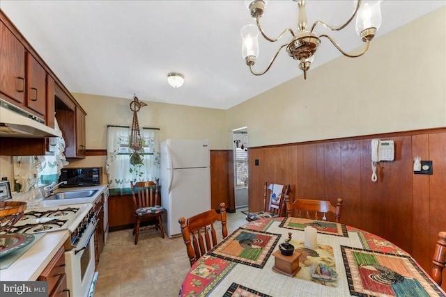 kitchen featuring an inviting chandelier, white appliances, under cabinet range hood, and wainscoting