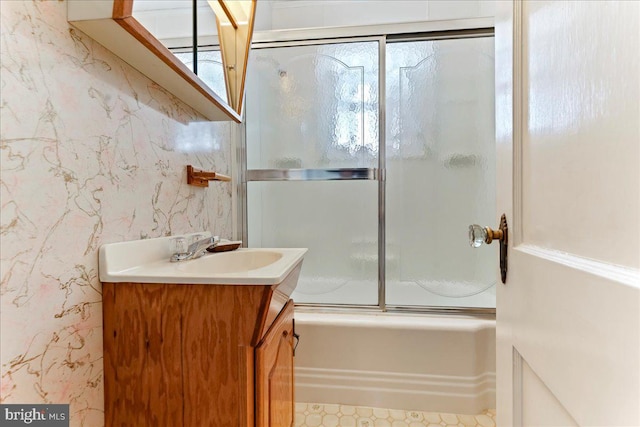 full bathroom with combined bath / shower with glass door, wallpapered walls, and vanity