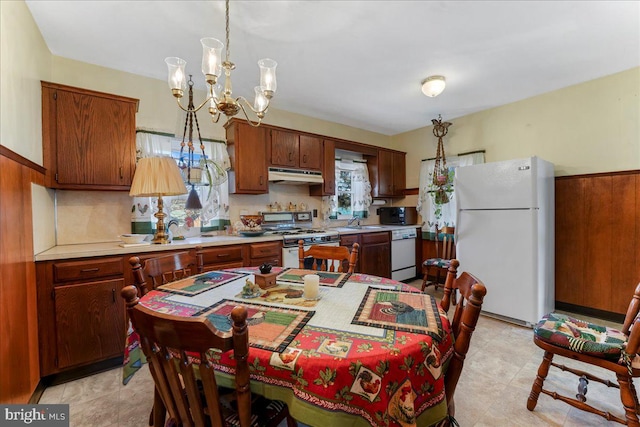 kitchen featuring under cabinet range hood, a sink, white appliances, an inviting chandelier, and light countertops