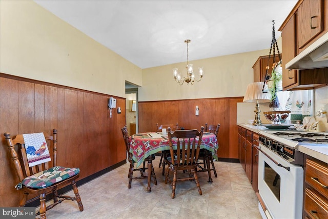 dining area with a chandelier, a wainscoted wall, and wood walls