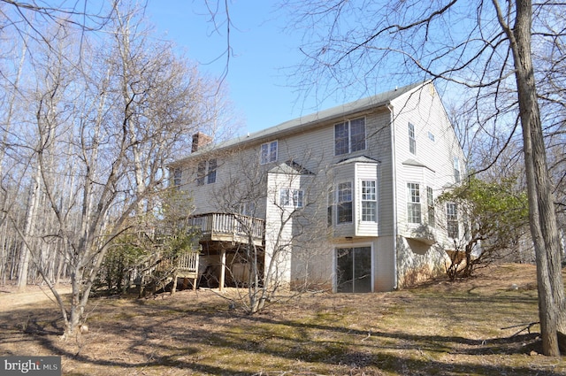 back of house with stairs, a deck, and a chimney