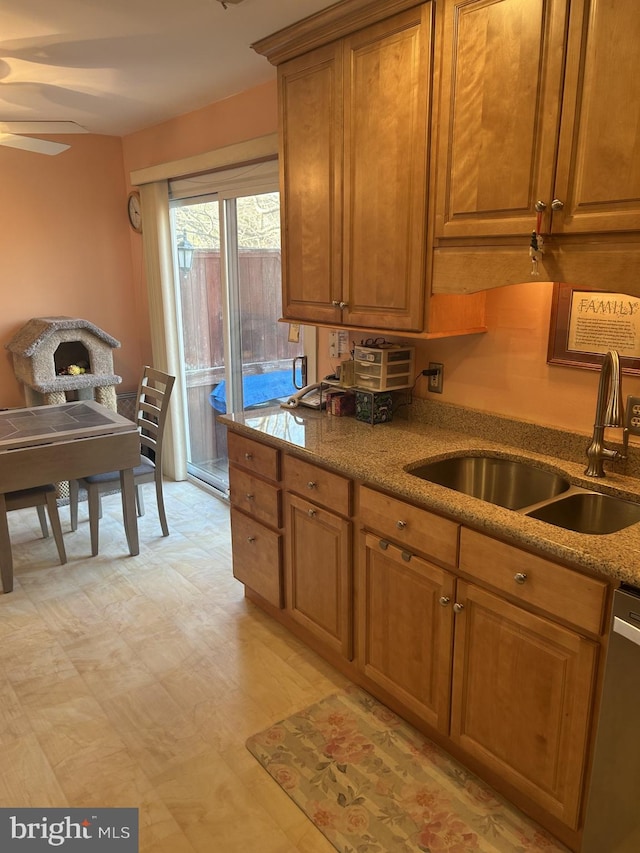 kitchen with brown cabinetry, stone counters, a sink, and stainless steel dishwasher