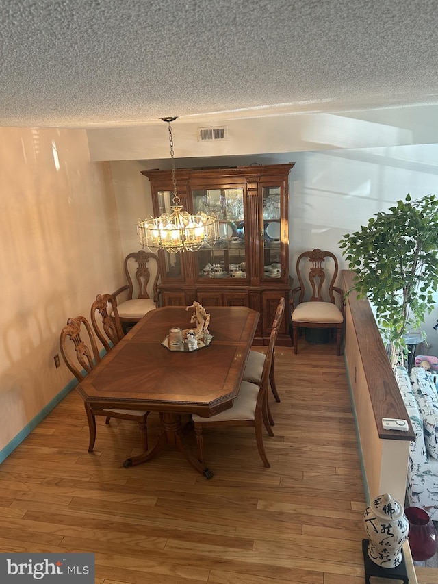 dining space featuring visible vents, a notable chandelier, light wood-style flooring, and a textured ceiling