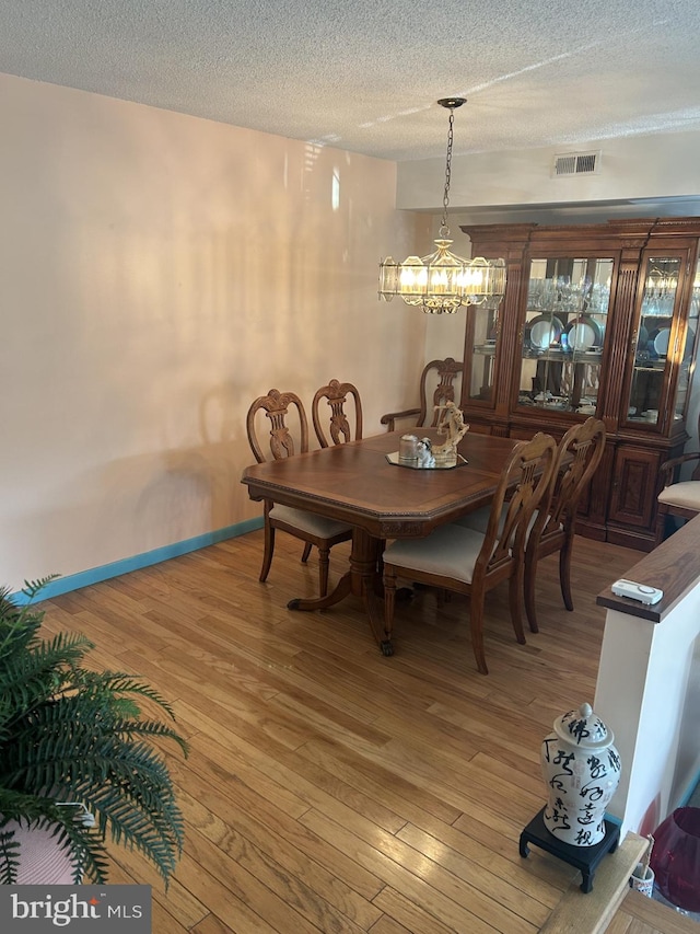 dining space featuring an inviting chandelier, light wood-style flooring, visible vents, and a textured ceiling