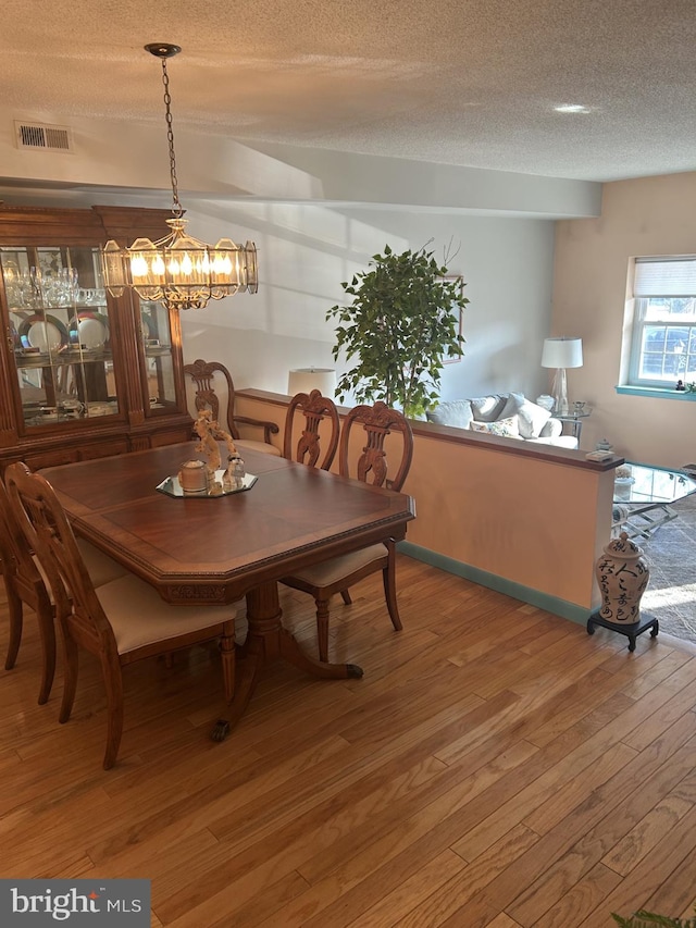 dining space featuring light wood-type flooring, visible vents, a textured ceiling, and baseboards