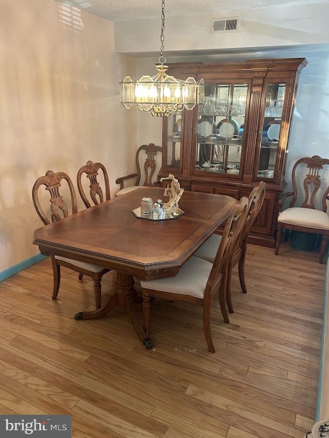 dining area with light wood-type flooring, visible vents, and a textured ceiling