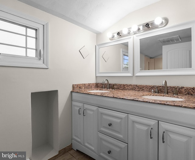 bathroom featuring lofted ceiling, double vanity, visible vents, and a sink