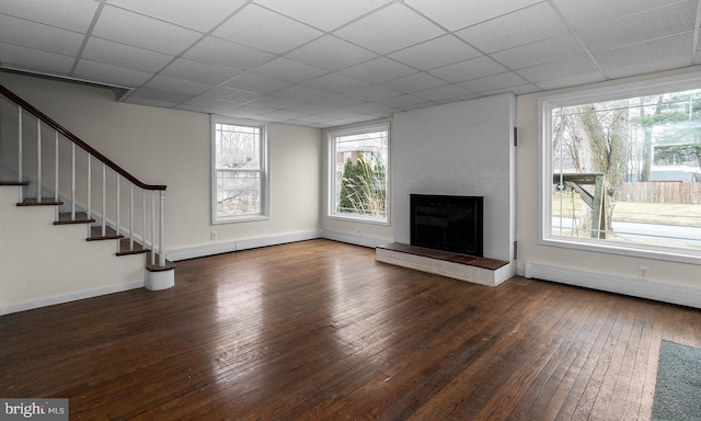 unfurnished living room featuring a paneled ceiling, a baseboard radiator, a large fireplace, hardwood / wood-style floors, and stairs