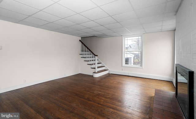 below grade area with a paneled ceiling, baseboards, stairway, and hardwood / wood-style floors