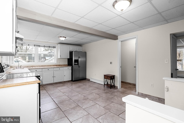 kitchen with light tile patterned floors, a paneled ceiling, light countertops, white cabinets, and stainless steel fridge