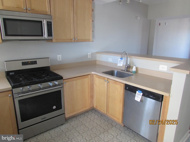 kitchen with appliances with stainless steel finishes, light countertops, a sink, and a peninsula