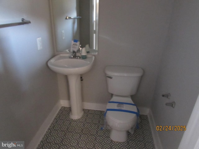 half bathroom with toilet, baseboards, a sink, and tile patterned floors