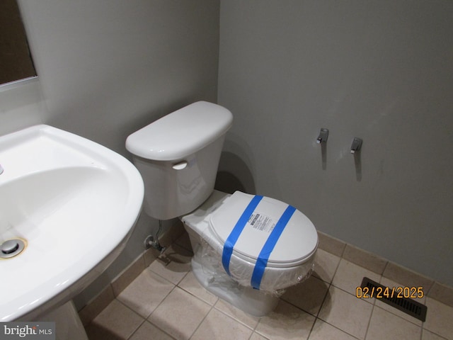 half bathroom featuring tile patterned flooring, baseboards, a sink, and toilet