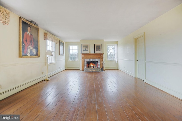 unfurnished living room featuring a baseboard radiator, a tile fireplace, and hardwood / wood-style flooring