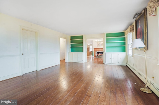 unfurnished living room with hardwood / wood-style flooring, a warm lit fireplace, built in shelves, and baseboard heating