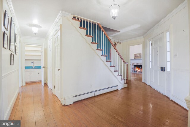 entrance foyer with a baseboard heating unit, ornamental molding, light wood-type flooring, and stairs